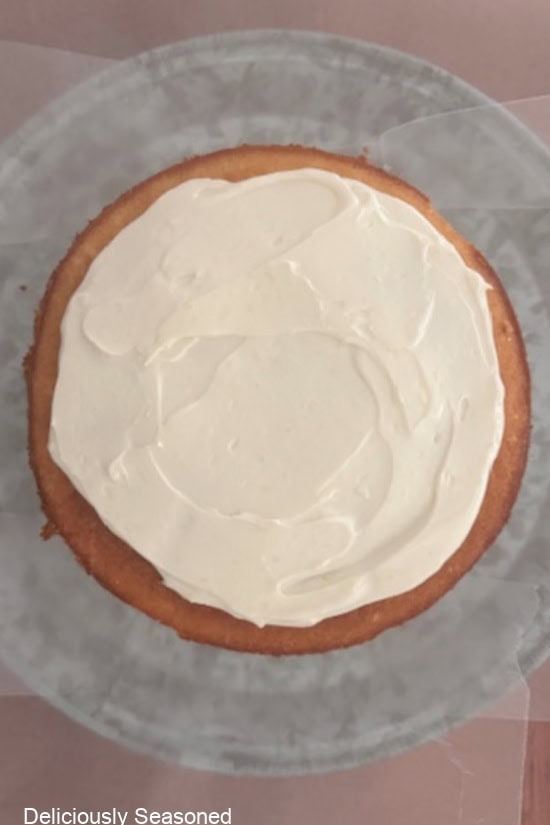 A round lemon cake with lemon cream cheese frosting spread on top of one of the cake layers.