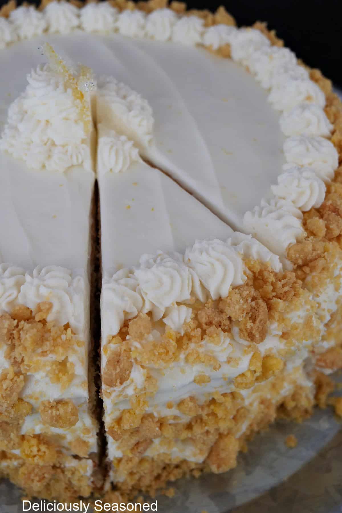 A lemon crunch layer cake completely decorated and a slice of cake cut out of the cake and not removed yet.