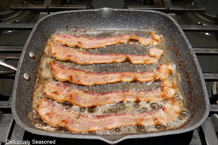 Five slices of bacon frying in a sallow frying pan.