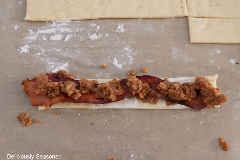A crescent strip of dough with streusel filling and a strip of bacon on it.