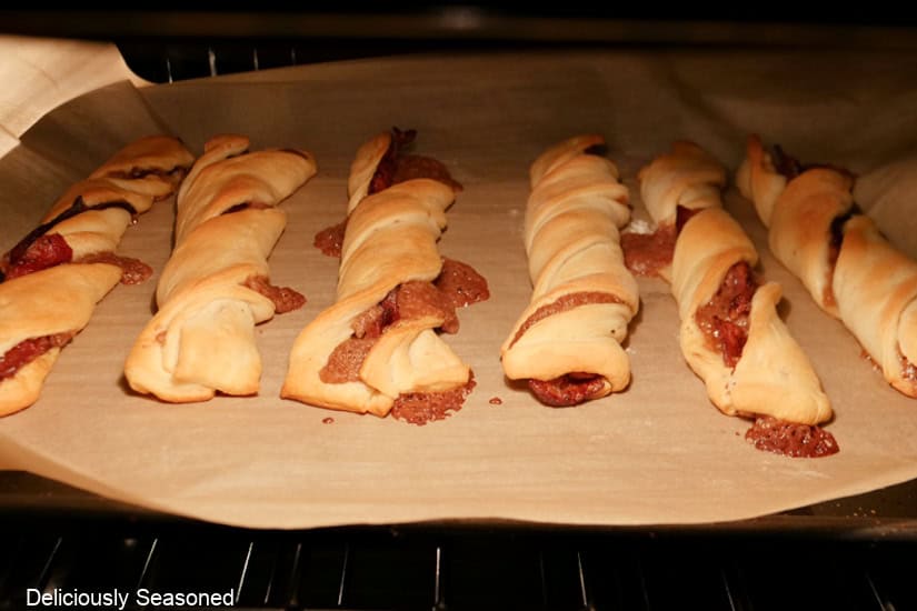 A baking sheet lined with parchment paper with six maple bacon twists on it baking in the oven.