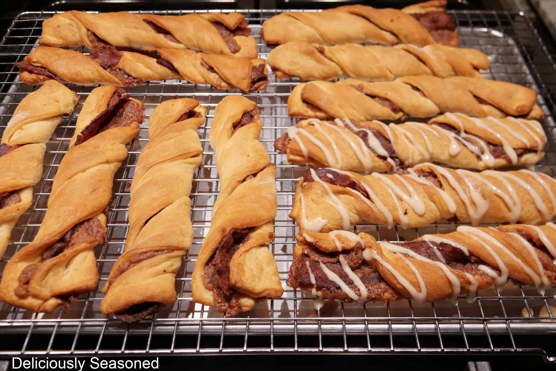 A wire rack placed over a baking sheet and maple icing being drizzled over the maple bacon twists.