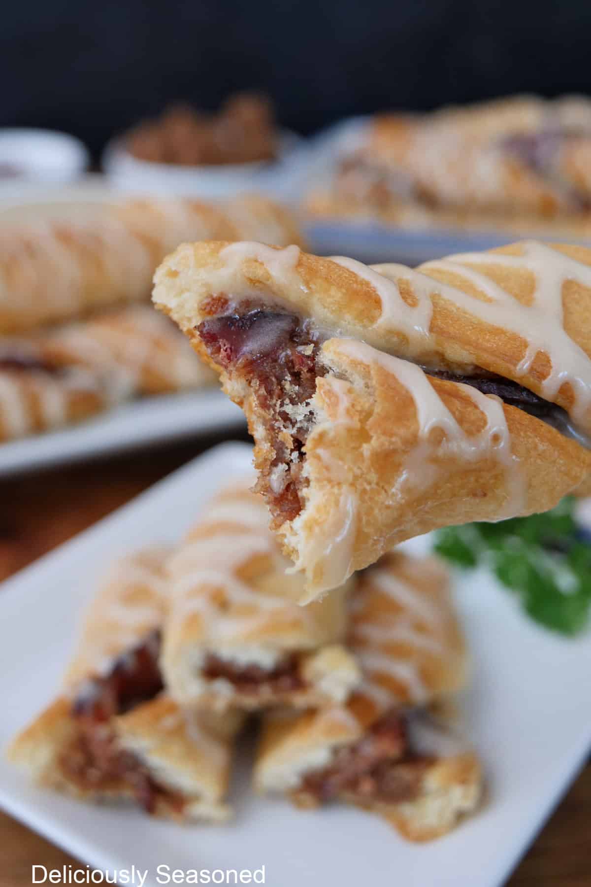A maple bacon twist held above others on a white plate with a bite taken out of it.