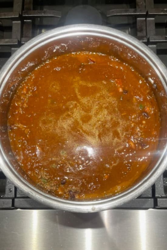 A silver pot with one pot chili simmering on the stove.