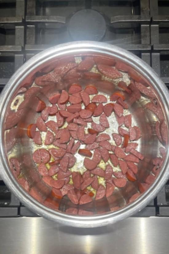 A silver pot with smoked sausage slices being cooked.