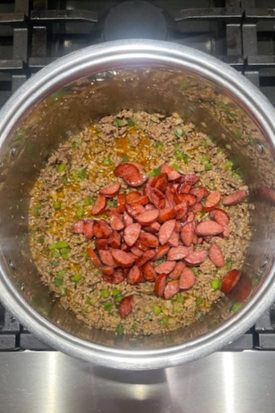 A silver pot with the sliced, cooked sausage added to the chili ingredients.