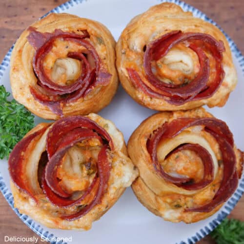 A round white plate with blue trim with four pepperoni crescent roll roses on it.