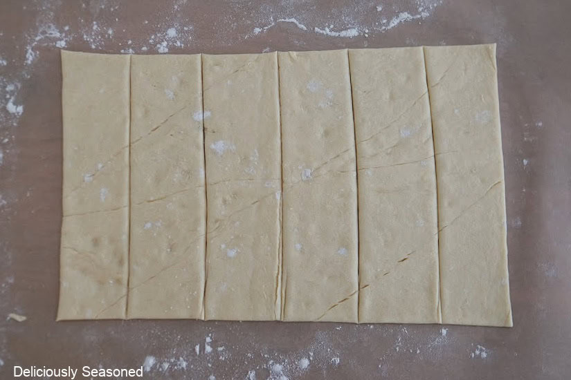 Parchment paper with six strips of crescent dough on it.