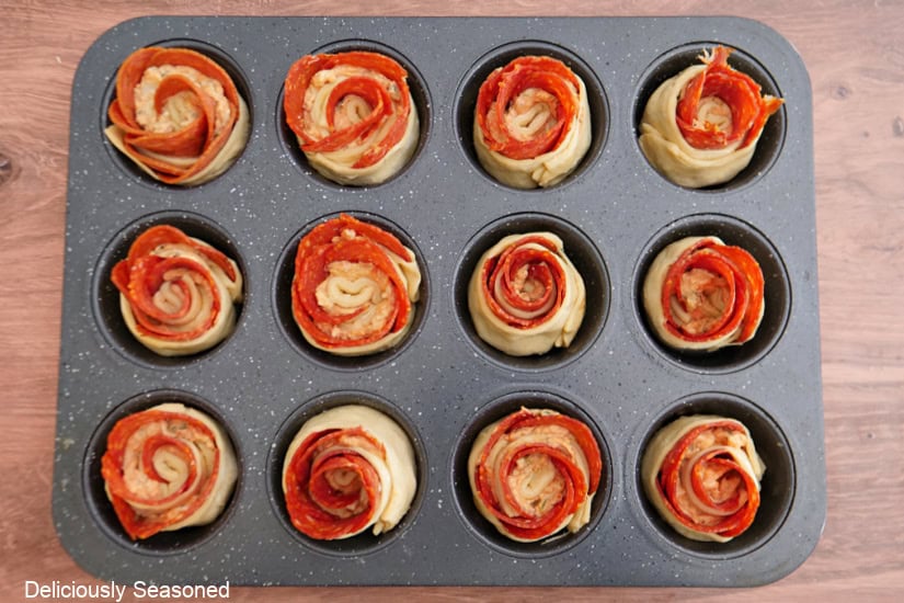 A 12-count muffin tin filled with pepperoni crescent roll roses before being baked.