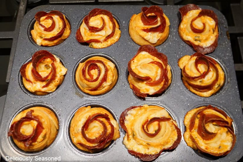 A 12-count muffin tin with baked pepperoni crescent roll roses in it after being baked.