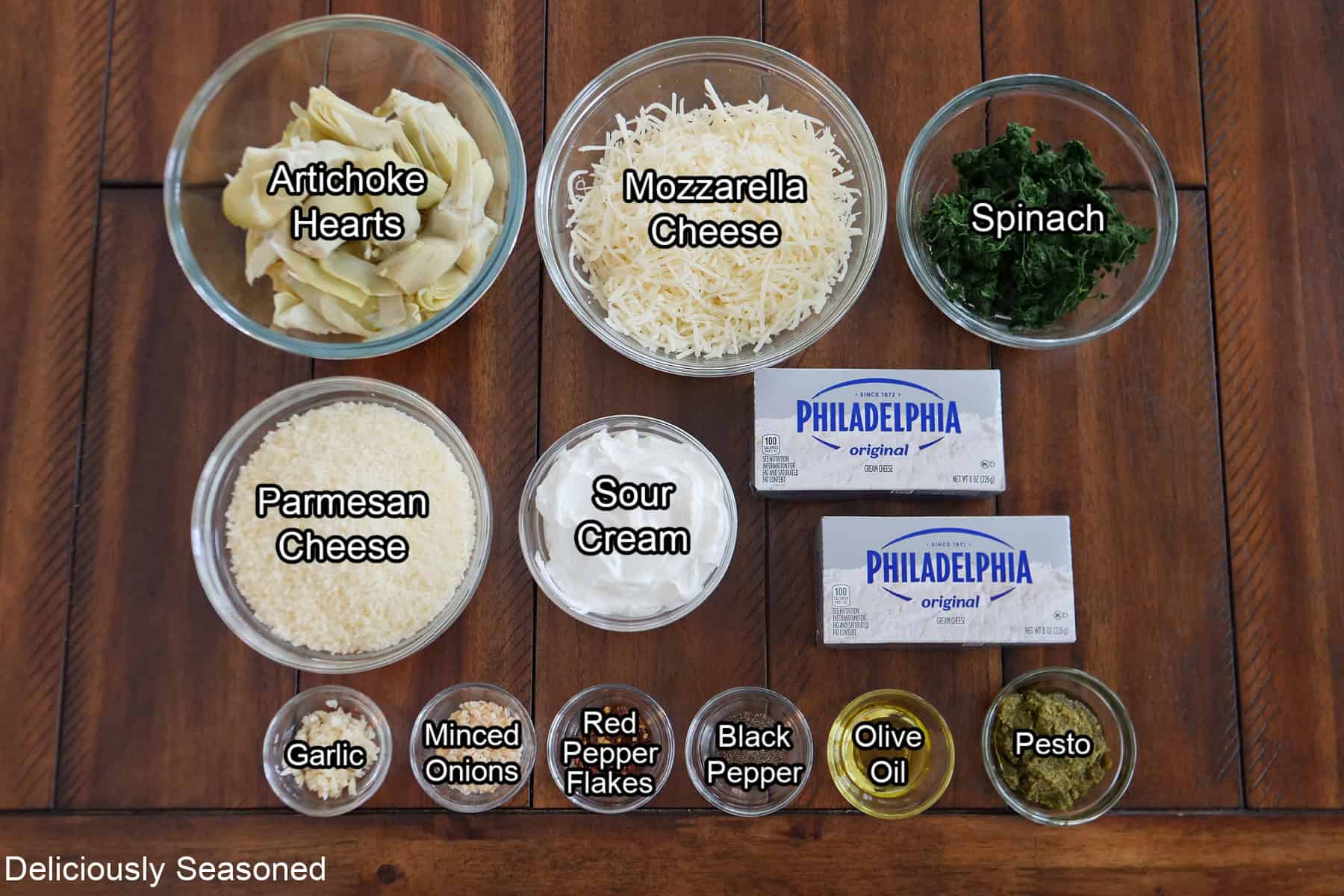 A wood surface with all the ingredients place on it for pesto spinach and artichoke dip.