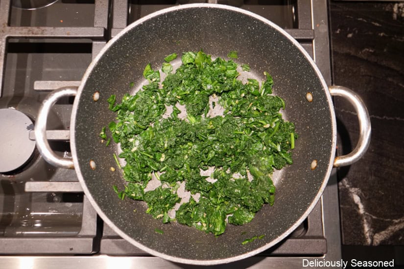A frying pan with roasted garlic and spinach in it.