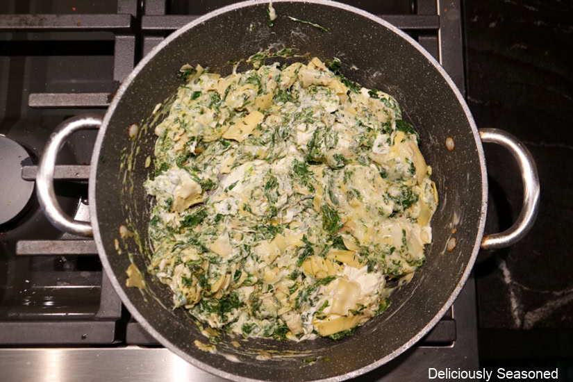 A frying pan with artichokes, spinach, and garlic in it.