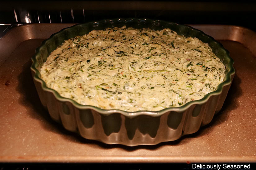 A green round baker with pesto spinach and artichoke dip in it and placed in the oven/broiler.