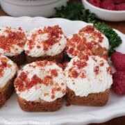 A white oval plate with mini cheesecake bites on it with raspberry crunch topping.