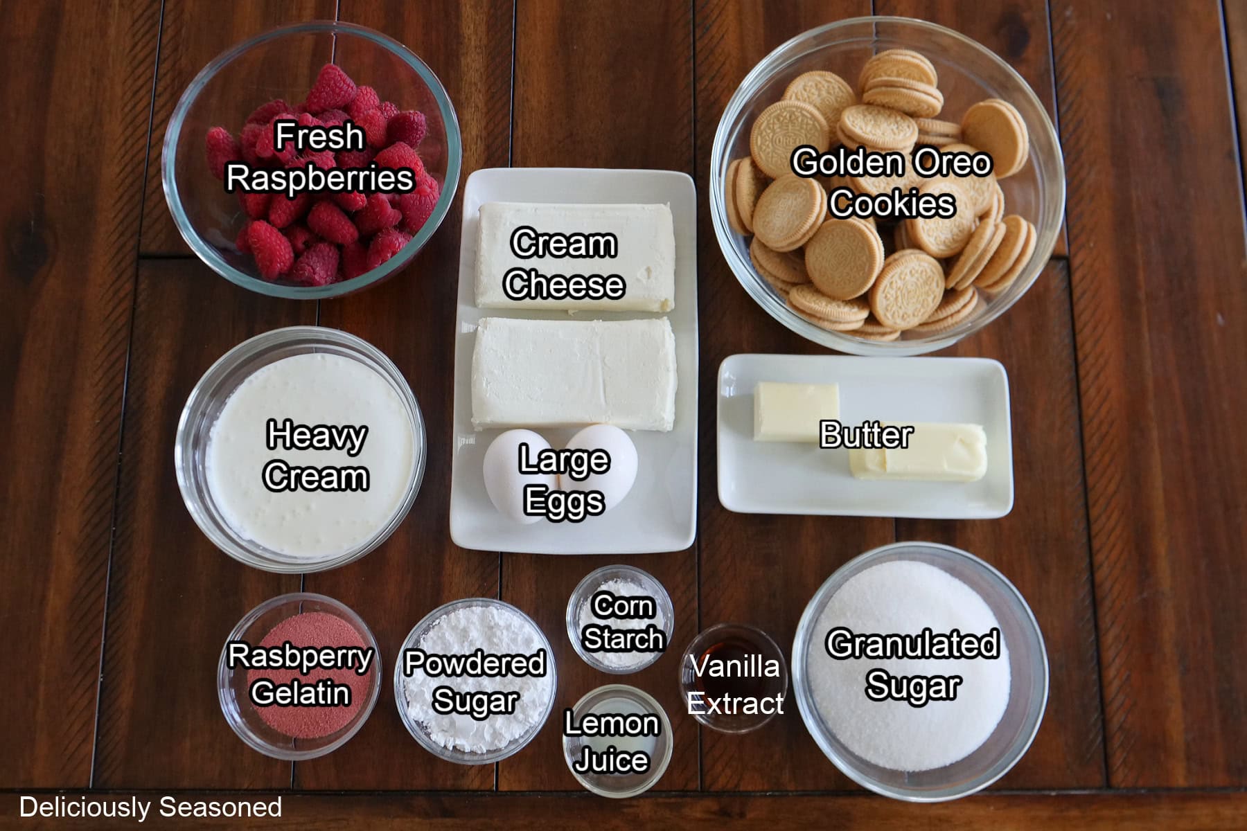 A wood surface with all the ingredients needed to make raspberry crunch cheesecake bites on it.