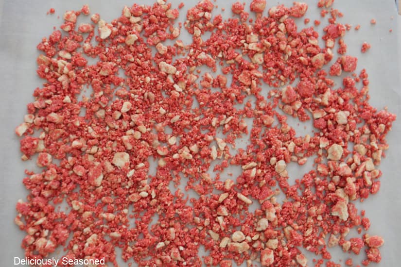 A parchment lined baking sheet with raspberry crunch crumbles layed out on it.