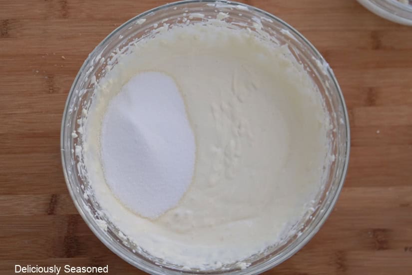 A wood surface with a glass bowl filled with cheesecake mixture.