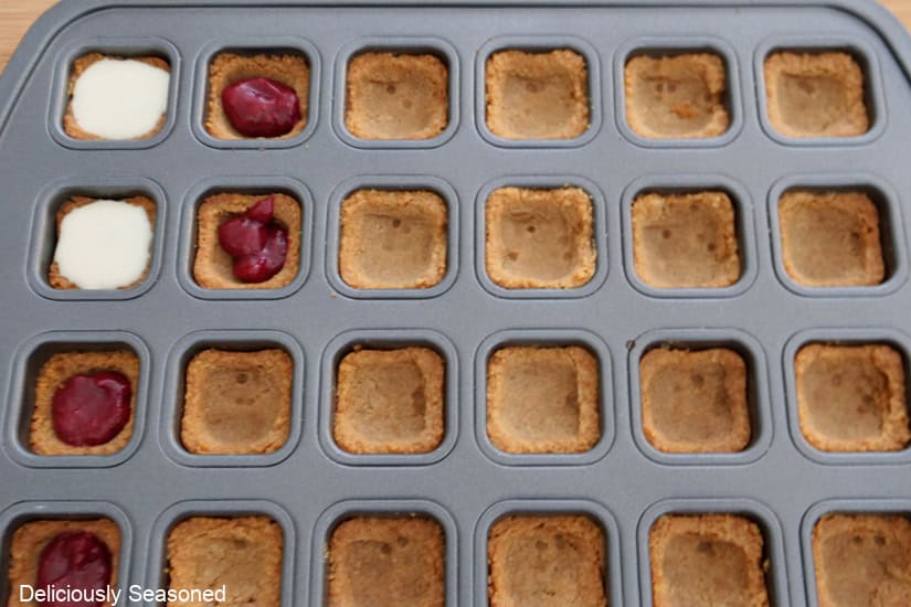 A 24-count mini muffin tin with raspberry filling and some with cheesecake mixture on top.