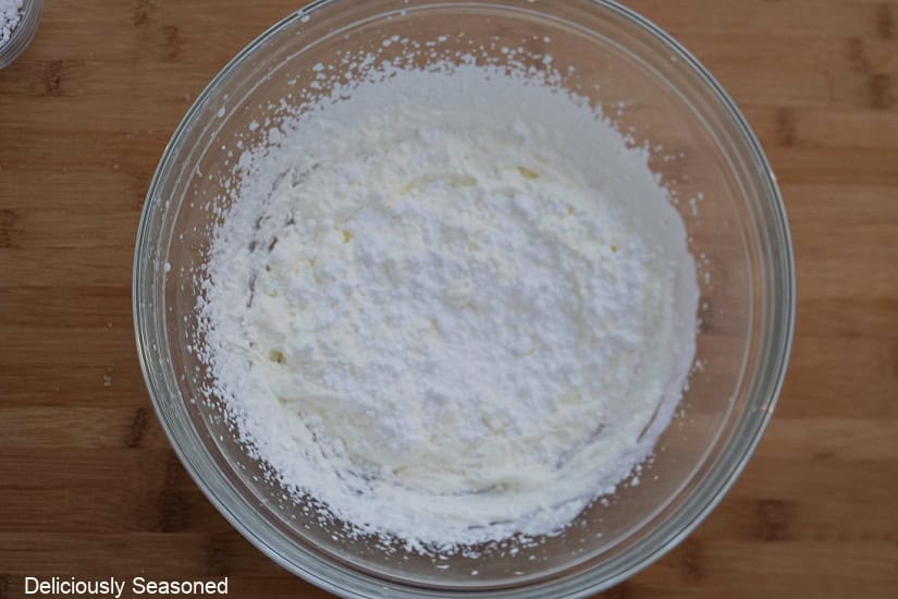 A wood surface with a glass bowl with the whipped cream ingredients in it.
