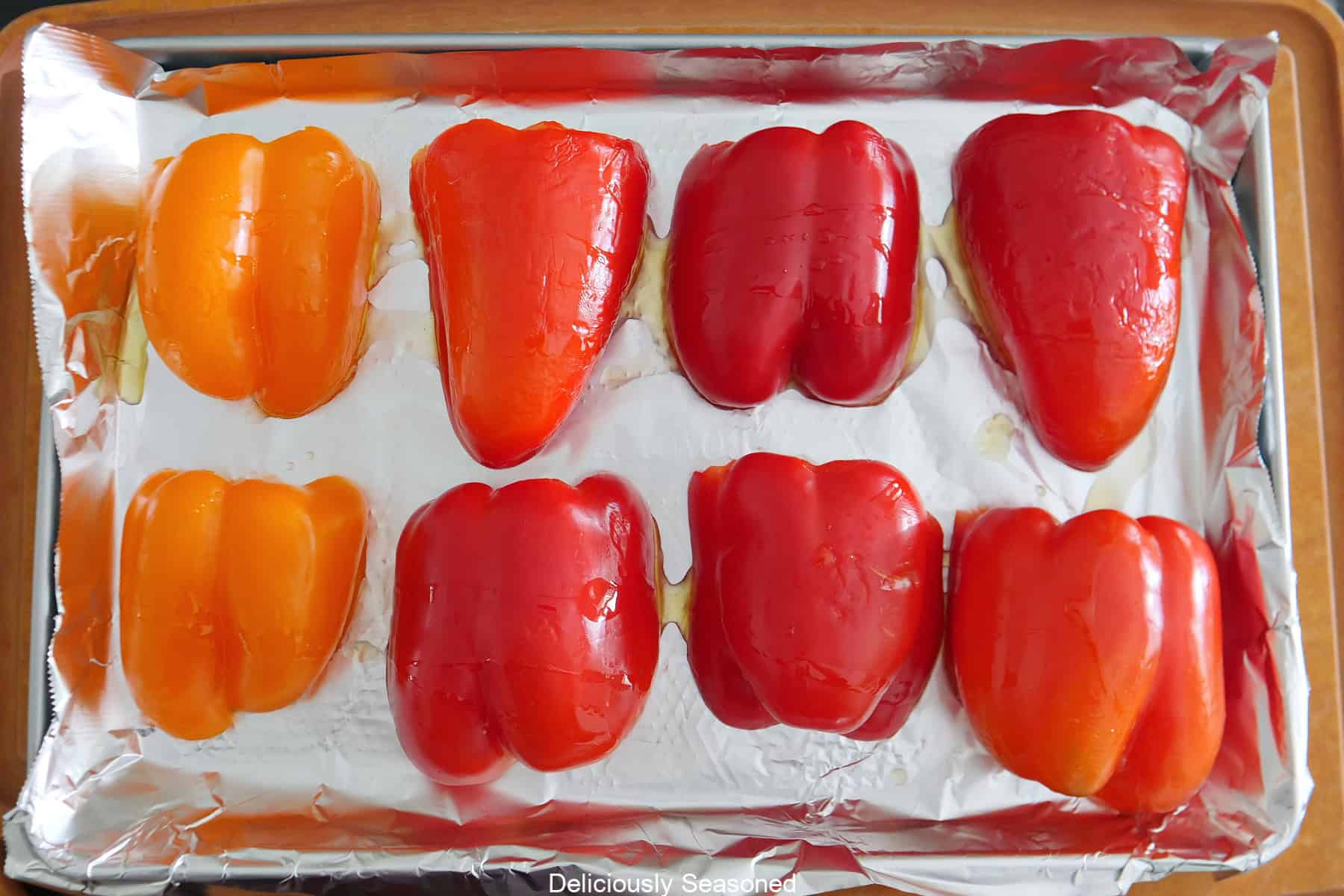 A foil lined baking sheet with 8 halves of bell peppers placed on it.