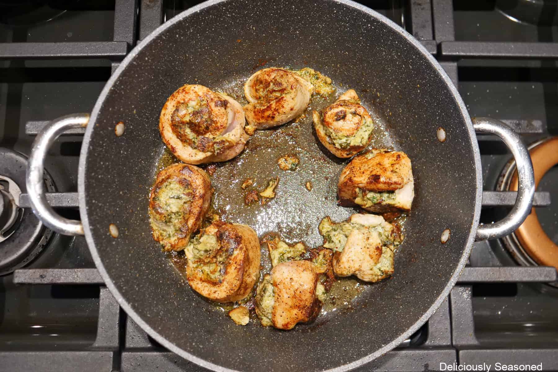 A frying pan with the rolled and stuffed chicken breasts being cooked on the stove.