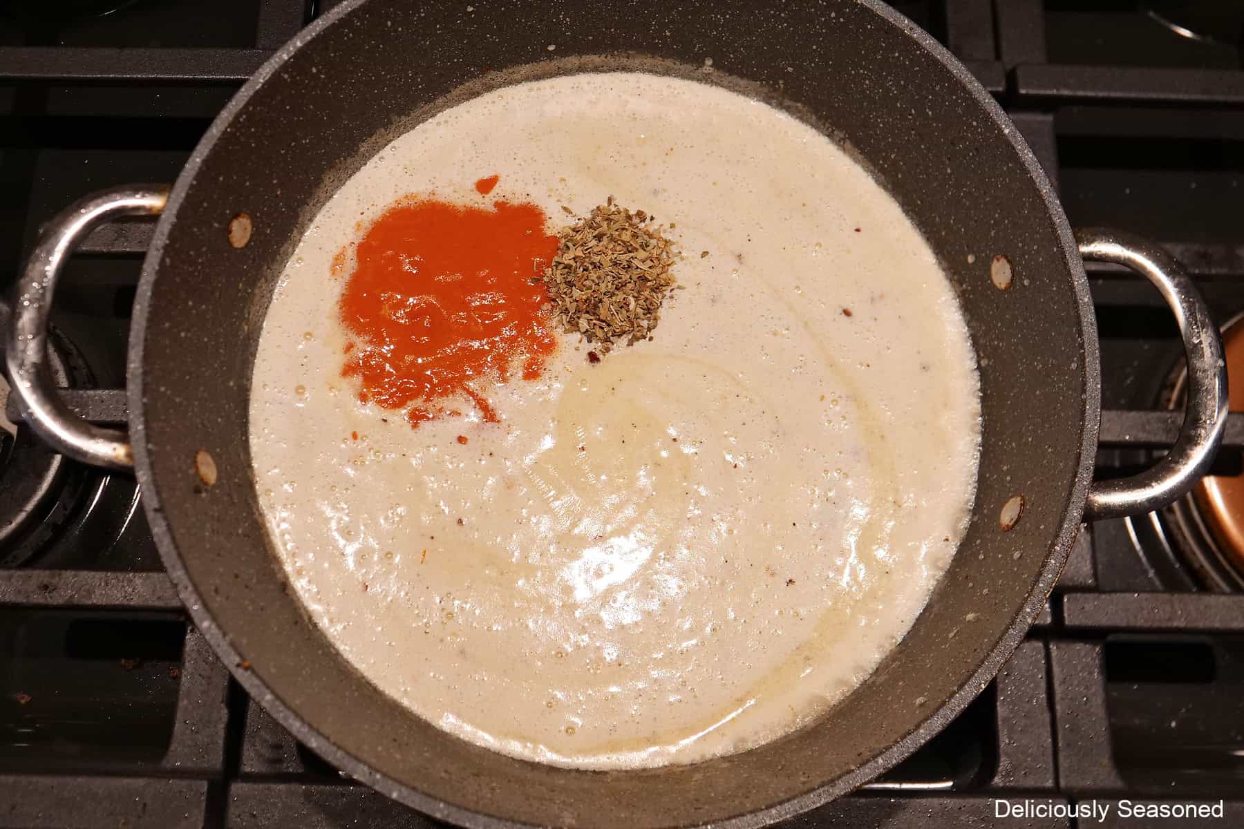 A frying pan with the heavy cream, garlic, butter, and seasonings in it.