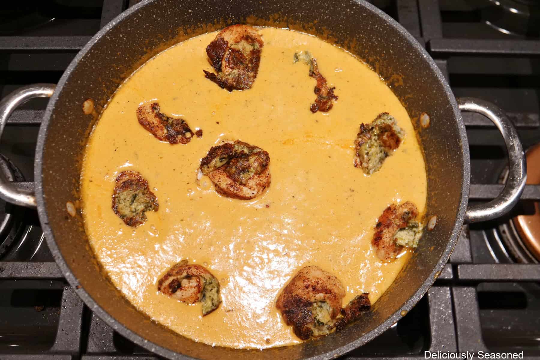 A frying pan with the creamy sauce and the cooked rolled up stuffed chicken in it.