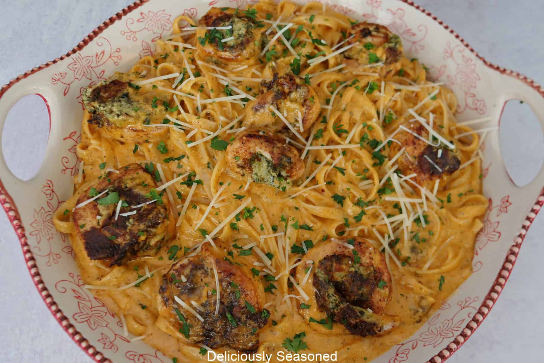 A ceramic bowl with fettuccine pasta, creamy sauce, cooked stuffed chicken, in the bowl and topped with shredded Parmesan.