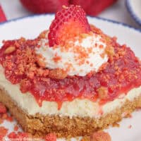 A white plate with blue trim with a strawberry cheesecake bar on it with a bite taken out of the corner.