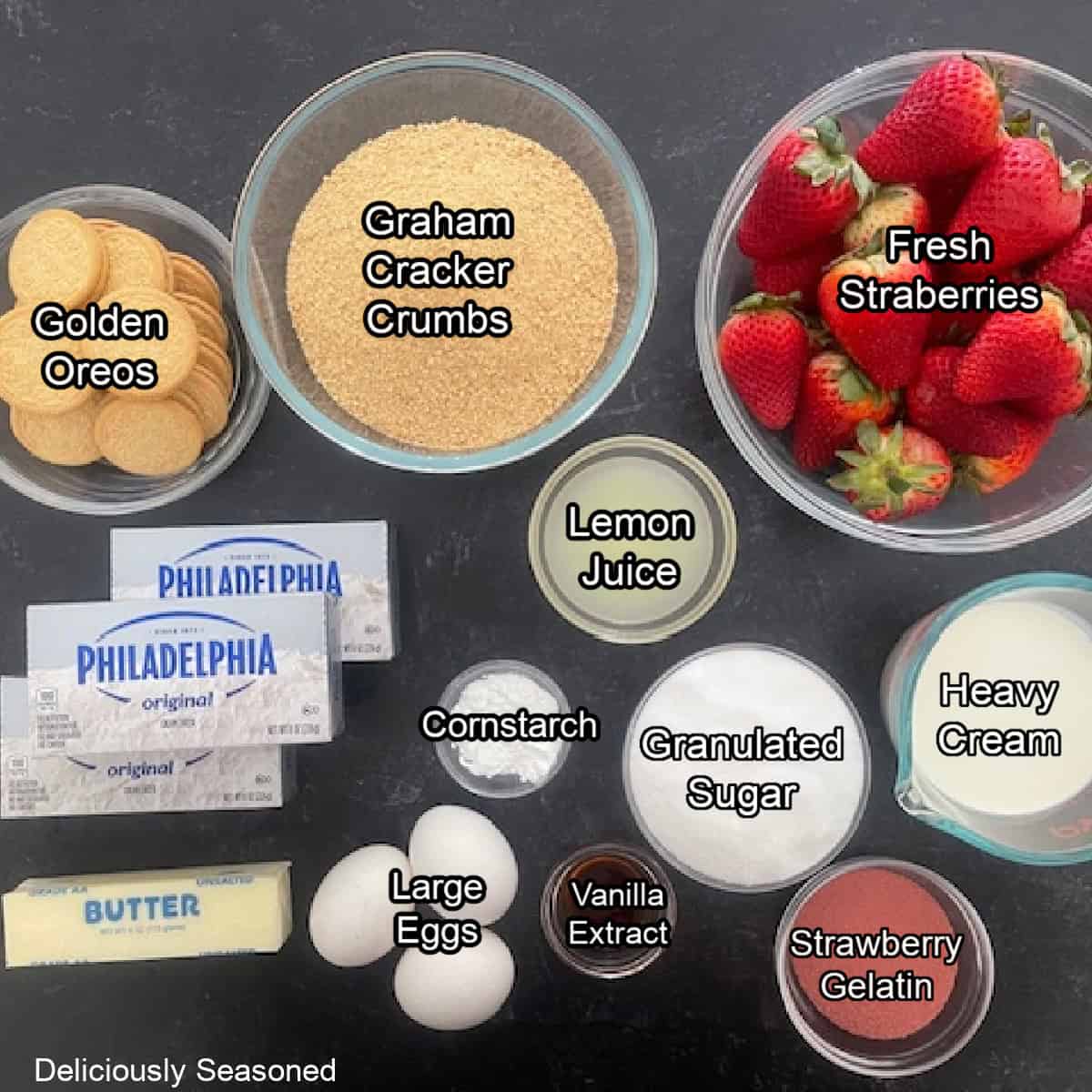 A dark surface with all the ingredients on it to make strawberry cheesecake bars.