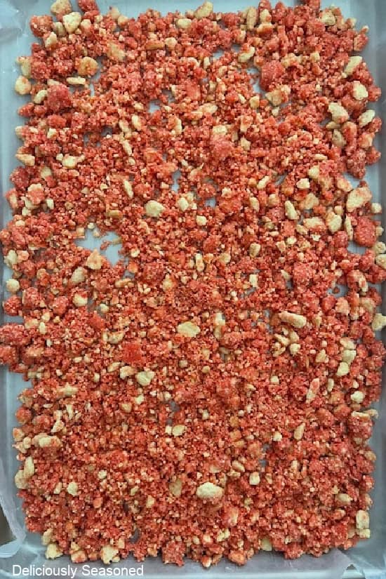 A baking sheet lined with parchment paper with the strawberry crunch laid out in a single layer.