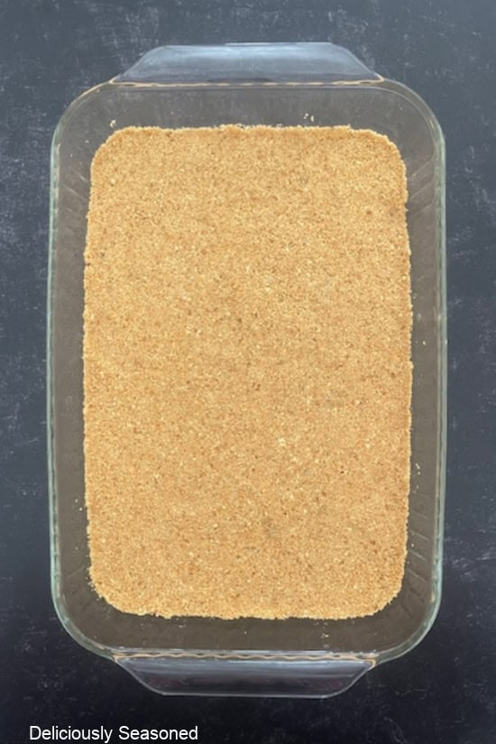 A 9x13 baking dish with a graham cracker crust in it before being baked.