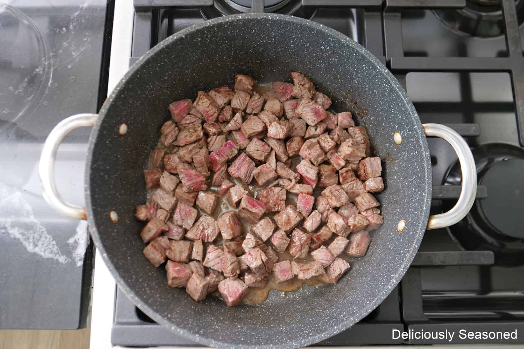 A frying pan with ribeye steak cut into bite-size pieces cooking in the pan.