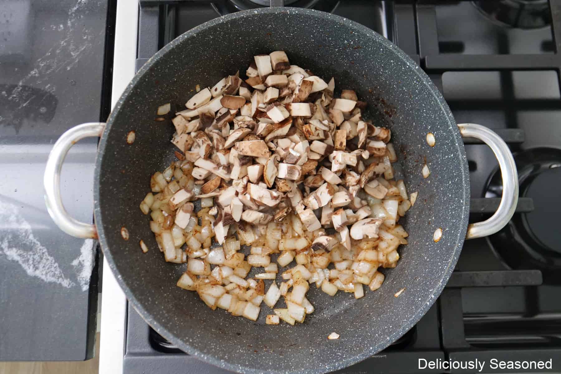 A frying pan with diced onions and mushrooms in it cooking.