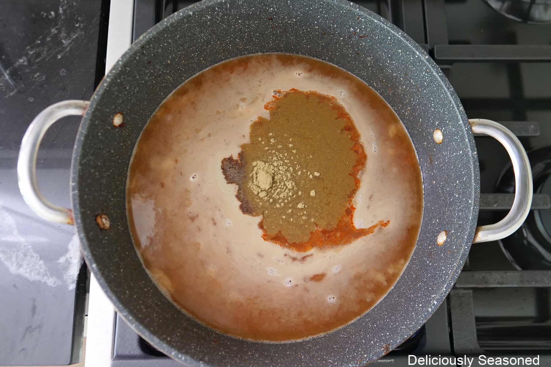 A pan with a roux, broth, and seasonings added before being mixed together.