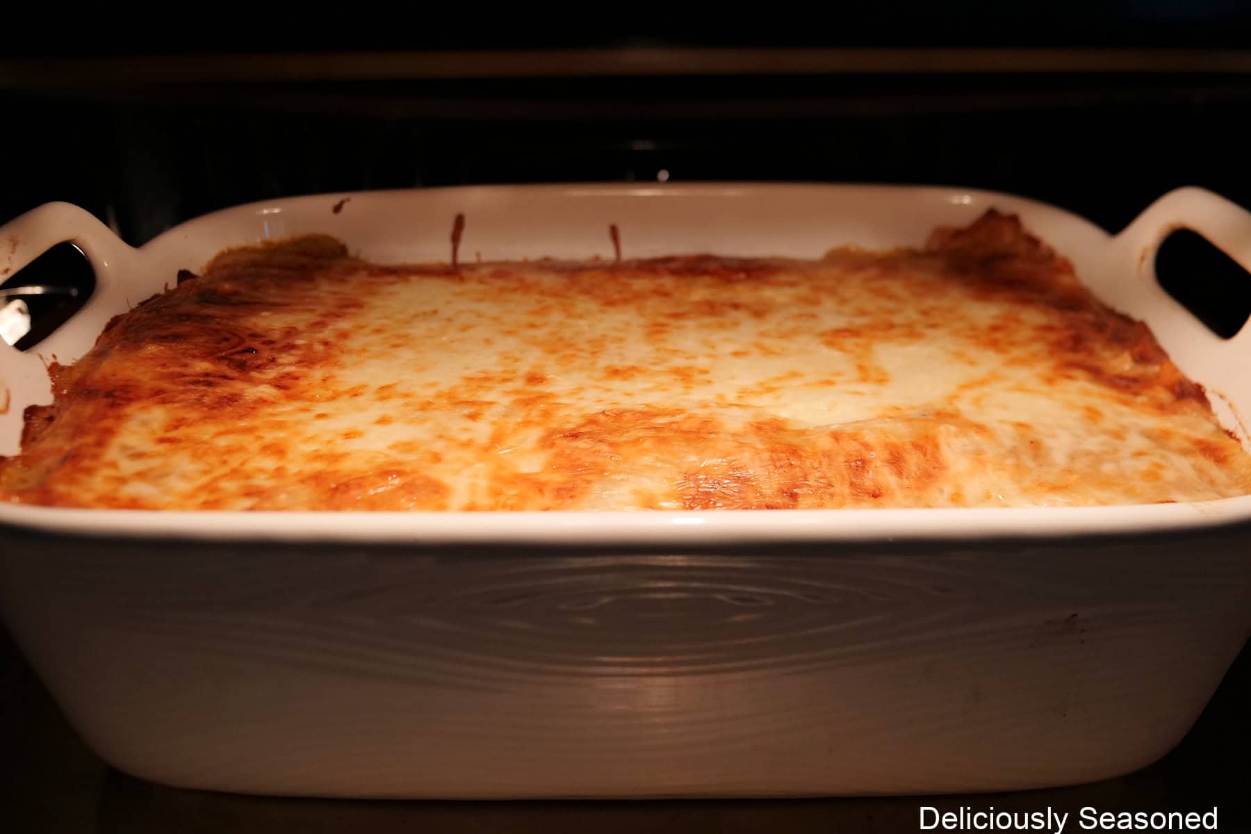 A white baking dish with beef stroganoff lasagna baking in the oven.