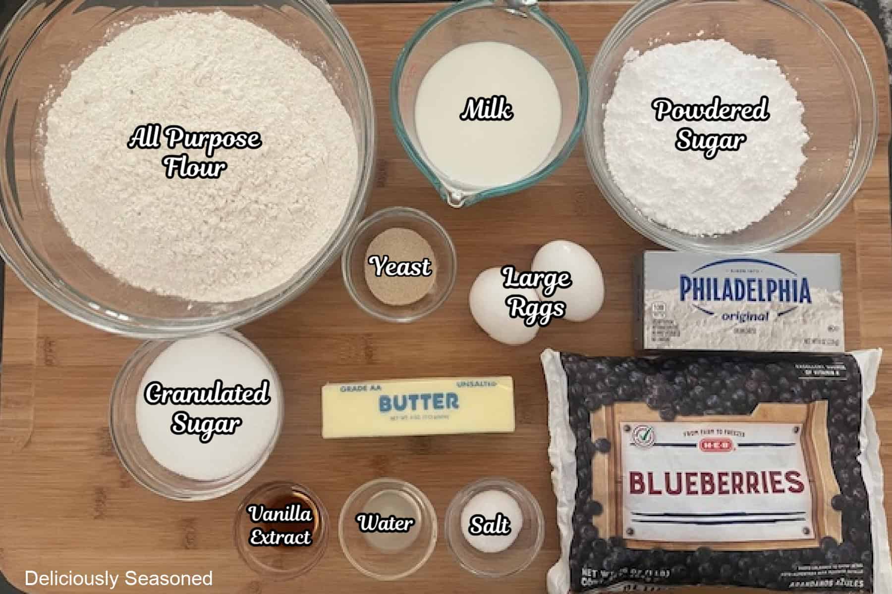 A wood surface with all the ingredients placed on it to make blueberry sweet rolls.
