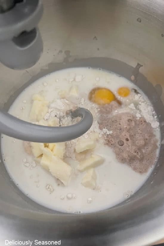 A mixing bowl with all the ingredients in it to make homemade dough with a dough hook in the bowl.