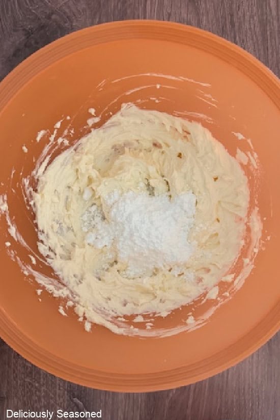 An orange mixing bowl with the cream cheese frosting ingredients in it being mixed together.