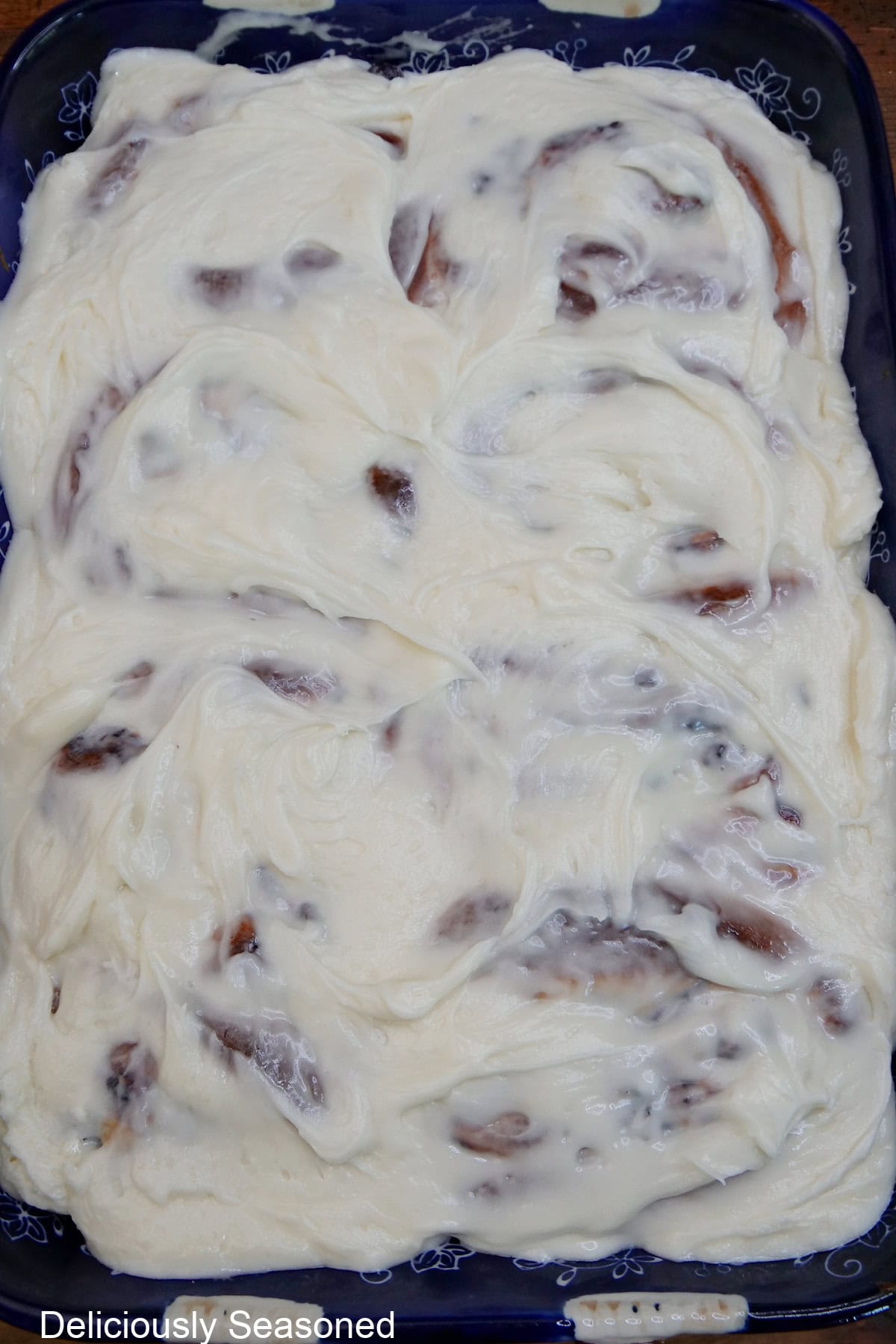 A 9 by 13 baking dish filled with baked sweet rolls and covered with cream cheese frosting.
