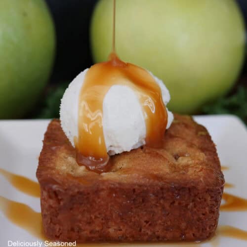 A white plate with a caramel apple blondie on it topped with vanilla ice cream and caramel drizzled over the top.