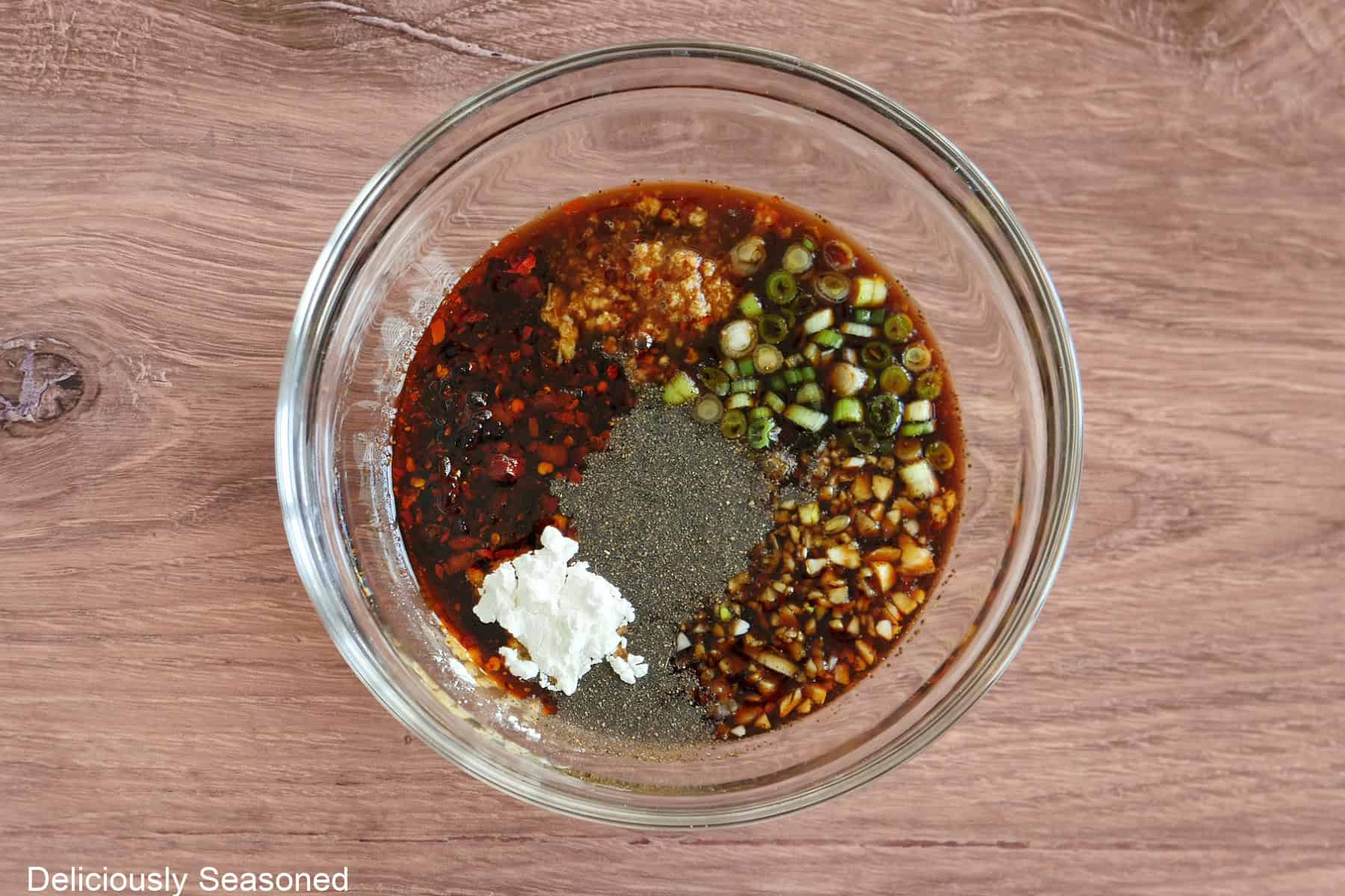 A wood surface with a glass bowl filled with all the ingredients placed in it to make the savory sauce for the chicken.