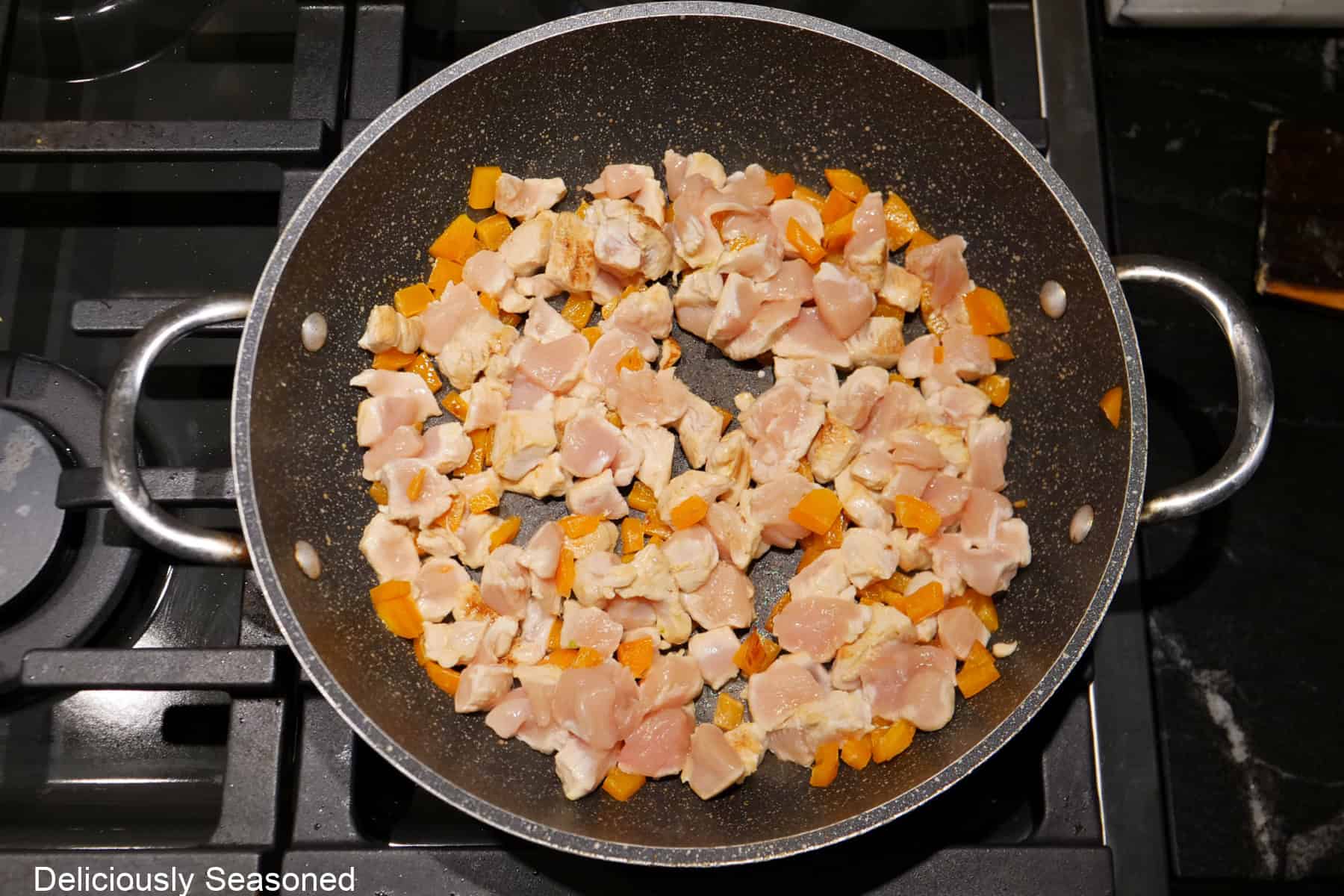 A pan with diced orange bell peppers and diced chicken breasts in it cooking.