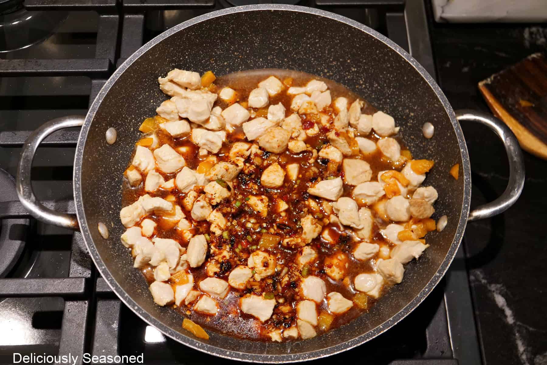 A sauce pan with browned chicken pieces and bell pepper with a chili sauce added to the pan.