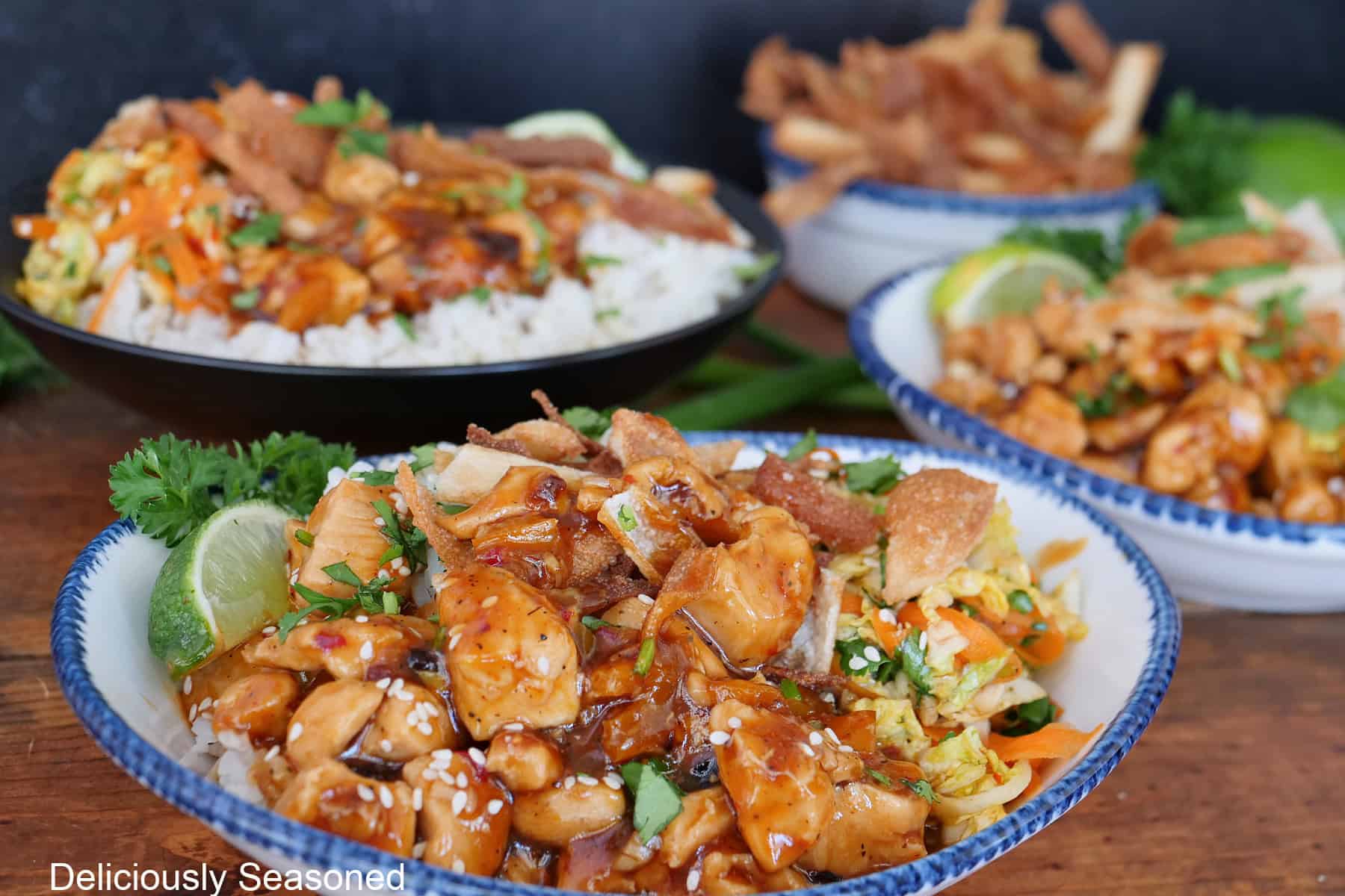 A wood surface with three white bowls with blue trim filled with chicken wonton.