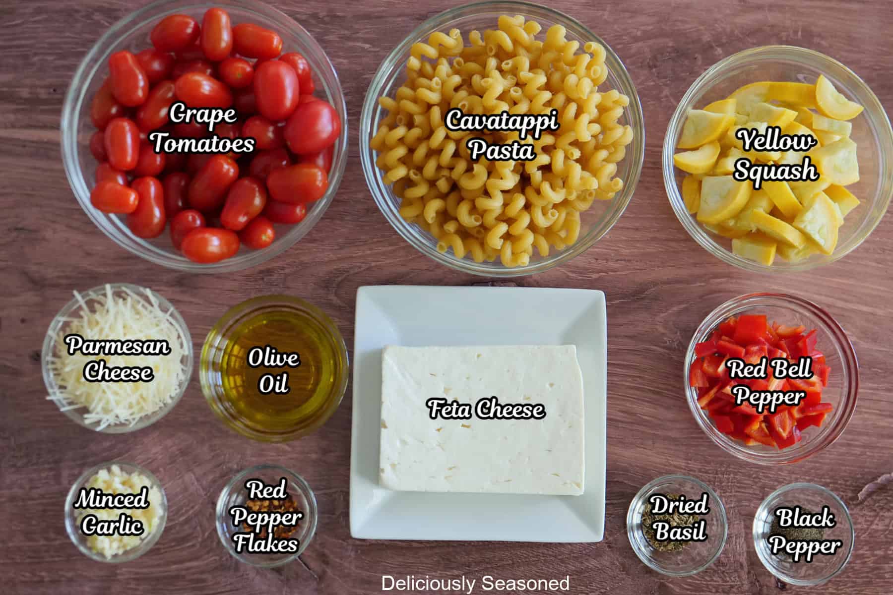 A wood surface with all the ingredients placed on it to make feta tomato pasta.