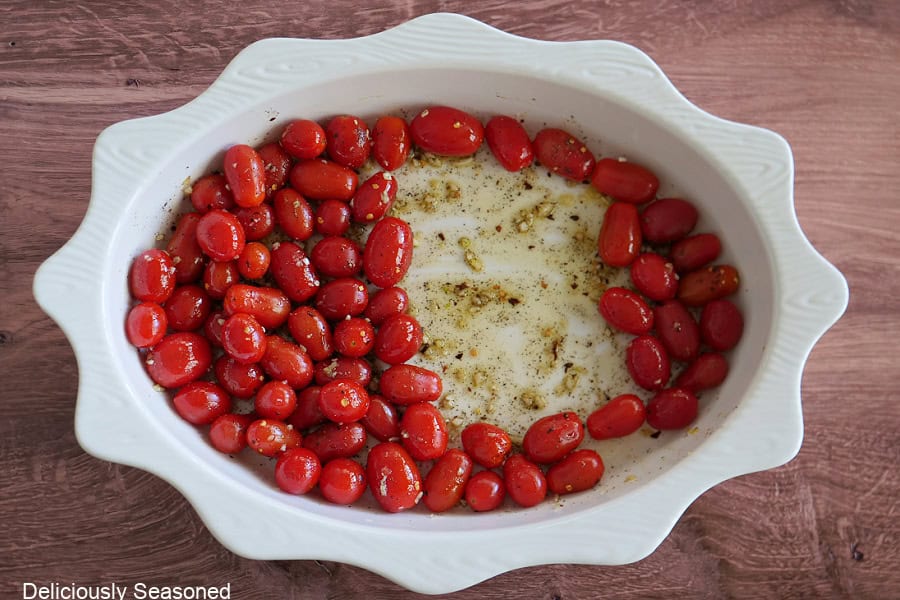 A white oval baking dish with grape tomatoes and seasonings in it.
