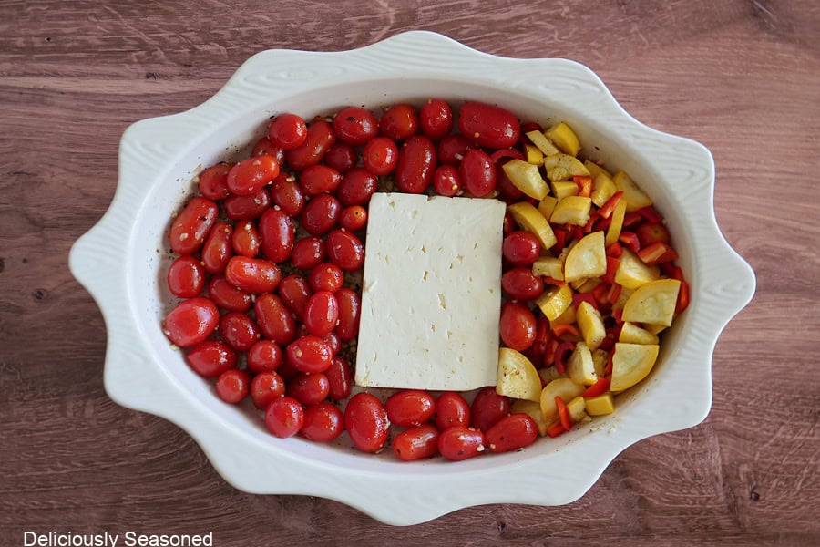 A white oval baking dish with grape tomatoes, feta cheese, and diced yellow squash in it.