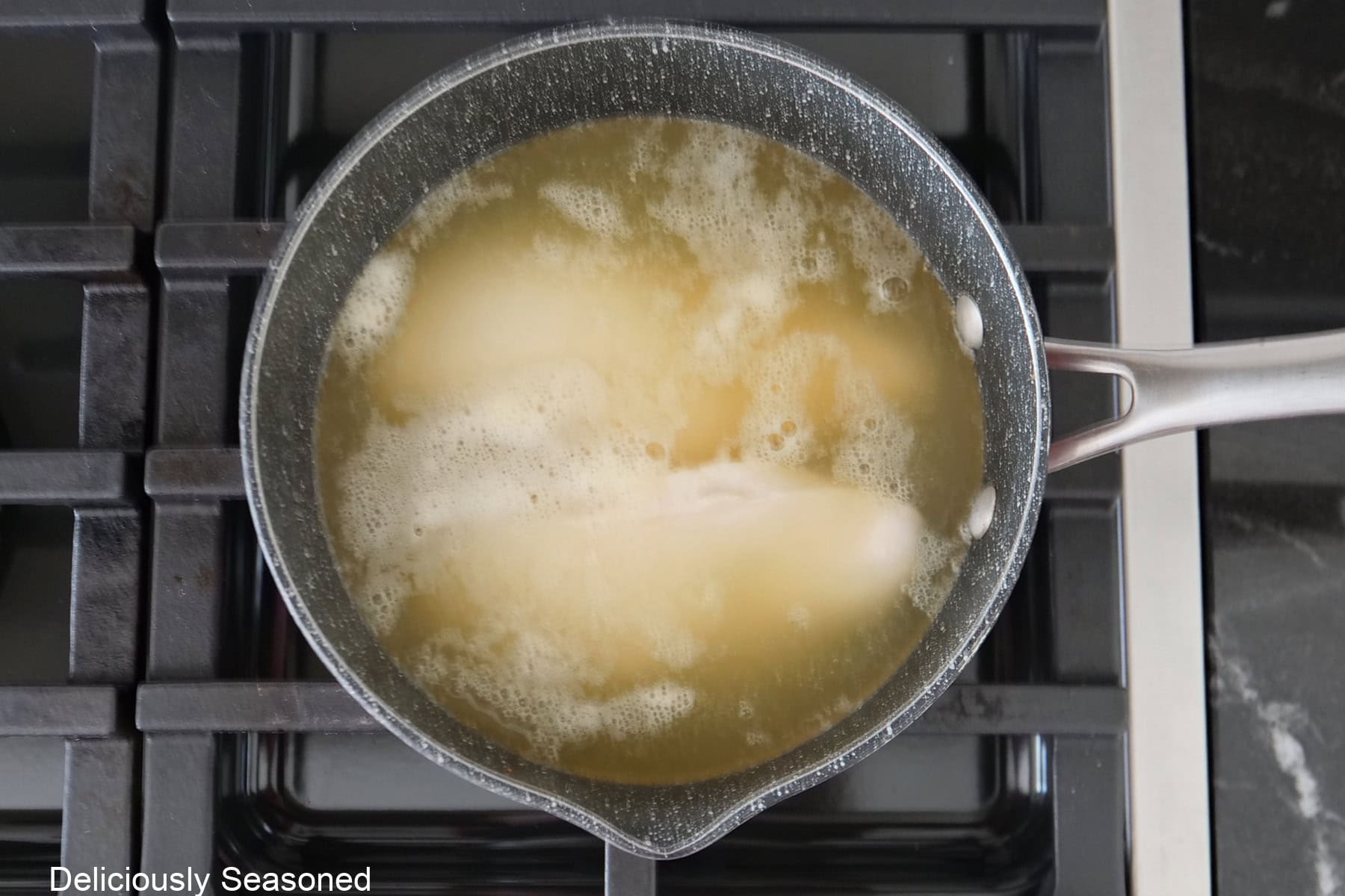A saucepan filled with chicken broth with two chicken breasts boiling in it.